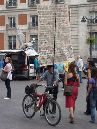 Madrid, Spain; May 23 2011. Elderly man showing a protest banner on a bicycle among the people at Puerta del Sol during the 15-M protests. Photography taken on May 23 2011 in Madrid, Spainのeditorial素材