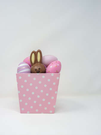 Pink basket with white polka dots filled with decorative eggs with a chocolate Easter bunny hidden inside. Vertical white backgroundの写真素材