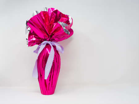 Giant chocolate Easter egg wrapped in pink silver foil with a pretty purple polka dot bow. Horizontal, white backgroundの写真素材