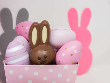 Chocolate Easter bunny hidden in a pink basket among decorative eggs, on a white background with...