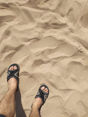 Feet with sandals walking on the sand of the beach