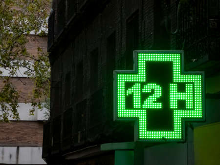 Luminous green pharmacy sign in an old building in Madrid in the early morning hoursの写真素材