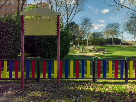 Blank sign at the entrance to a playground in the city, with a rest area with benches and buildings in the backgroundの写真素材