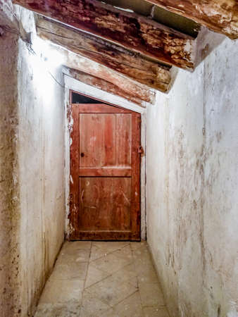 A mysterious, worn door at the end of a corridor in an abandoned and dirty garretの写真素材