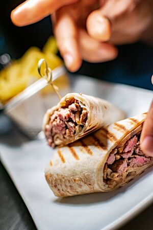a grilled steak tortilla wrap along side a portion of French fries being given the finishing touches...