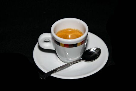 A cup of freshly grounded espresso coffee alongside a plate and spoonの写真素材