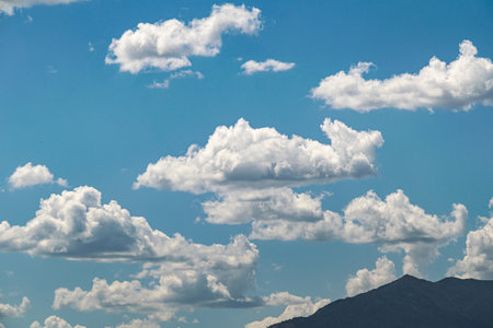 a collection of fluffy white clouds against blue skies and a mountain top silhouette
