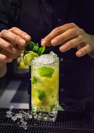 a alcoholic mojito cocktail getting the finishing garnish touches in a bar by a bartenderの写真素材