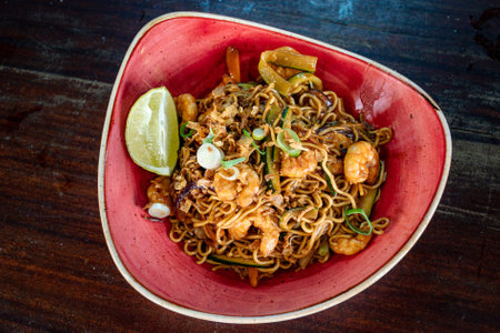 a birds eye view of a Thai style prawn noodles served in a red bowl.