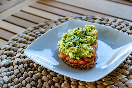a close up image of a slice of brown toast topped with grated tomatoes and smashed avocado