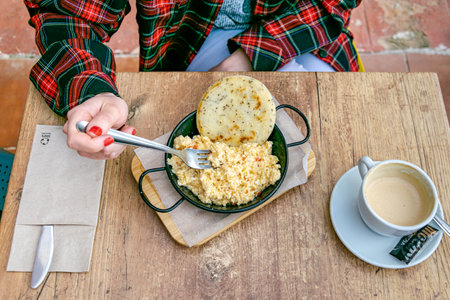 an image overlooking a women eating Colombian scrambled eggs with arepa served with a coffeeの写真素材