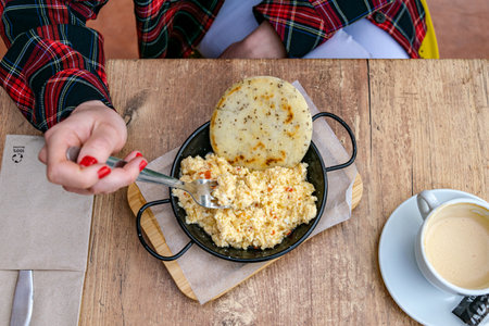 a close up overlooking a women eating Colombian scrambled eggs with arepa served with a coffeeの写真素材