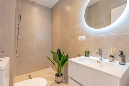 a close up image of a stone tile bathroom with illuminated mirror and standing shower in mediterranean holiday homeの写真素材