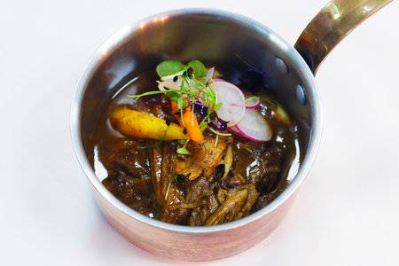slow cooked pulled lamb shoulder in a coper pot with baby carrots and slice radish