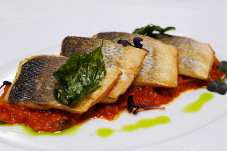 mediterranean pan seared sea bass fish fillet with tomato saffron sauce and basil in a white plateの写真素材
