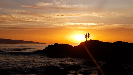 Silhouette of a man and a woman fishing at sunset on the beachの写真素材