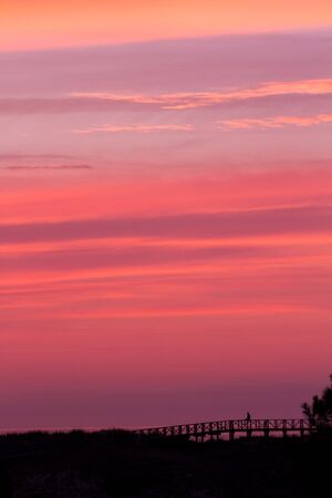 nice reddish sky at sunset. A silhouette of a person watches the show from a bridge in backlightの写真素材