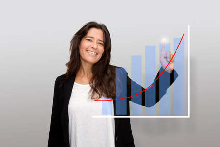 Attractive laughing middle-aged woman points a finger at charts of her business success. Positivism. Things are going very wellの写真素材