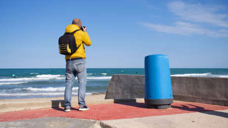 Unknown man with his photography equipment taking pictures on the beach on a sunny day with blue skyの写真素材
