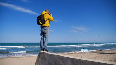 Unknown man with his photography equipment taking pictures on the beach on a sunny day with blue skyの写真素材