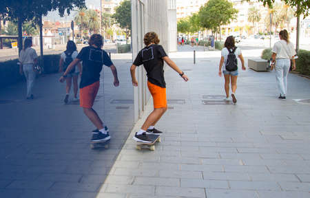 A boy skates on the street and sees his reflection in a glass window.