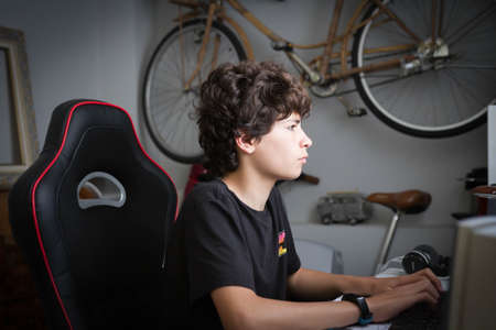 A serious, focused teenager in his room working from a computer