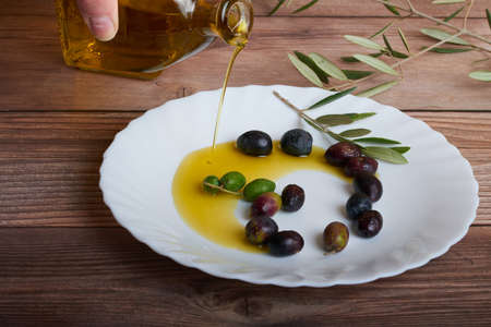 A bottle of oil with several ripe olives on a white plateの写真素材