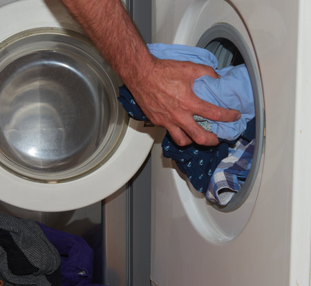 A man's hand putting clothes into a washing machineの写真素材