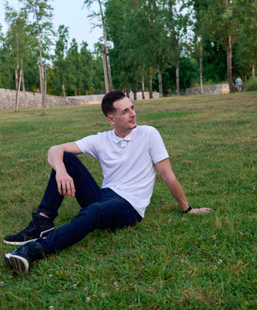 An attractive young man sitting on the grass in a park.の写真素材
