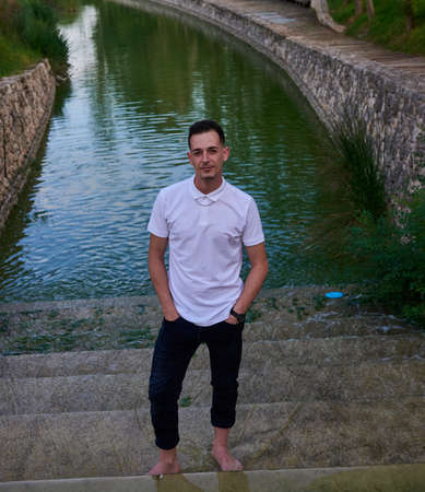 A young man in a white T-shirt posing inside a canal.