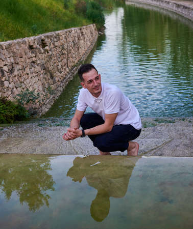 A young man in a white T-shirt inside a pond.の写真素材