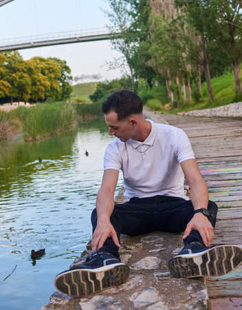 An attractive young man sitting on the bank of a canal in a park.の写真素材