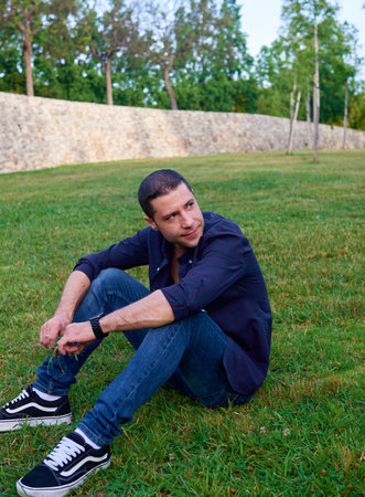 A young man posing relaxed on the grass in a park.の写真素材