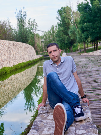 A young model in jeans sitting next to a canal in a park.の写真素材