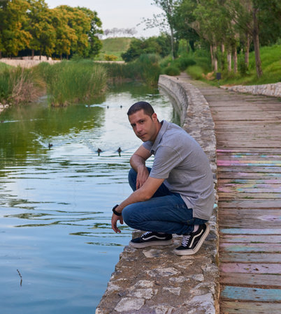An attractive young man sitting on the bank of a canal in a park.の写真素材