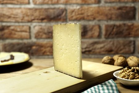 portion of spanish manchego cheese on cutting board with nuts and bricks backgroundの写真素材