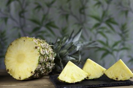 triangular pineapple slices on slate dish and half pineapple on  vegetation and wood backgroundの写真素材