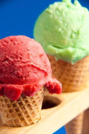 two ice cream cornet close-up green and strawberry colour on blue backgroundの写真素材