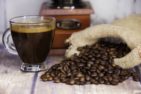 cup of coffee, coffee beans coming out of a sack and coffee grinder on wooden table