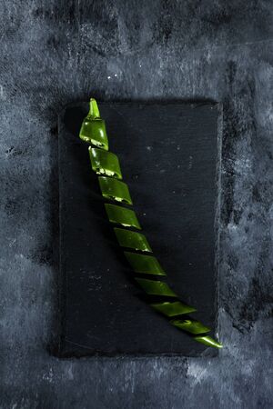 fresh spicy green pepper sliced on slate board on dark background from above. Top view