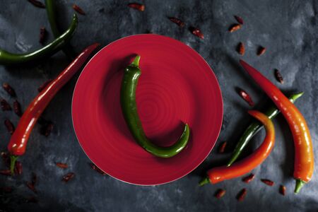 fresh spicy green pepper on red ceramic plate and various fresh red and green spicy peppers and cayenne peppers on dark background from above. Top viewの写真素材
