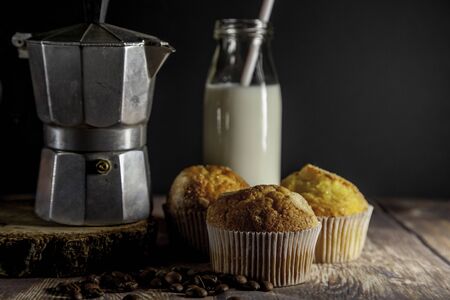 Italian coffee maker, muffins and fresh milk in a glass bottle on wooden table and blackの写真素材