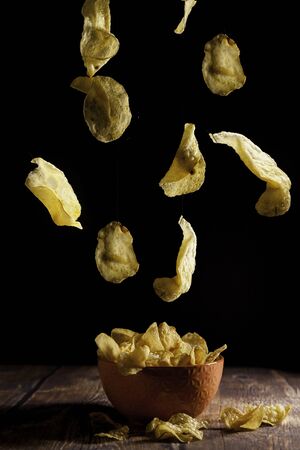 Potato chips falling into an orange ceramic bowl on a wooden table and blackの写真素材