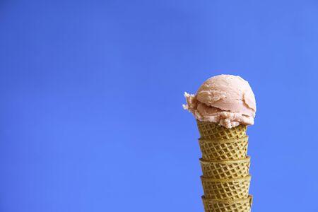 strawberry ice cream ball on waffle cornet on blue background. Copy space