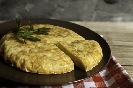 Spanish omelette and portion in a plate with napkin on wooden table and dark backgroundの写真素材