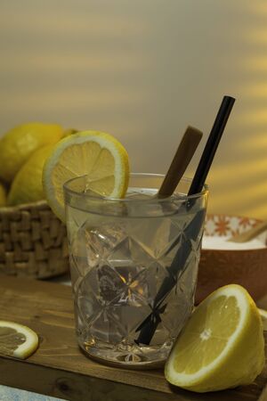 lemonade glass with ice, spoon and straw on cutting board, cut lemons and basket with lemons on background with sunlight entering through rear window. Copy spaceの写真素材