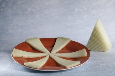 six slices of typical spanish manchego cheese on red ceramic plate and piece manchego cheese on blue...