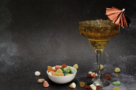 Iced tea cocktail glass with umbrella and jelly beans bowl on dark background with copy spaceの写真素材