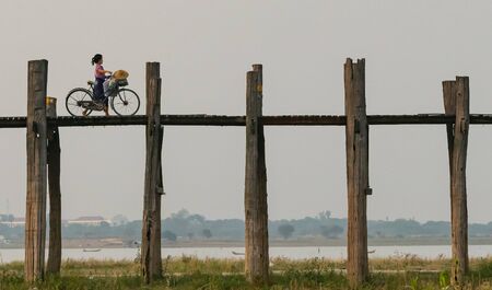 Mandalay, Myanmar. April 22, 2018. Young lady crossing U Bein Bridge with a bicycle in Mandalay regionのeditorial素材