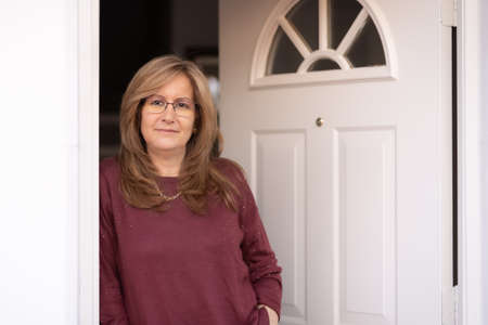 Mature white woman at the door of her house in a happy attitude.の写真素材
